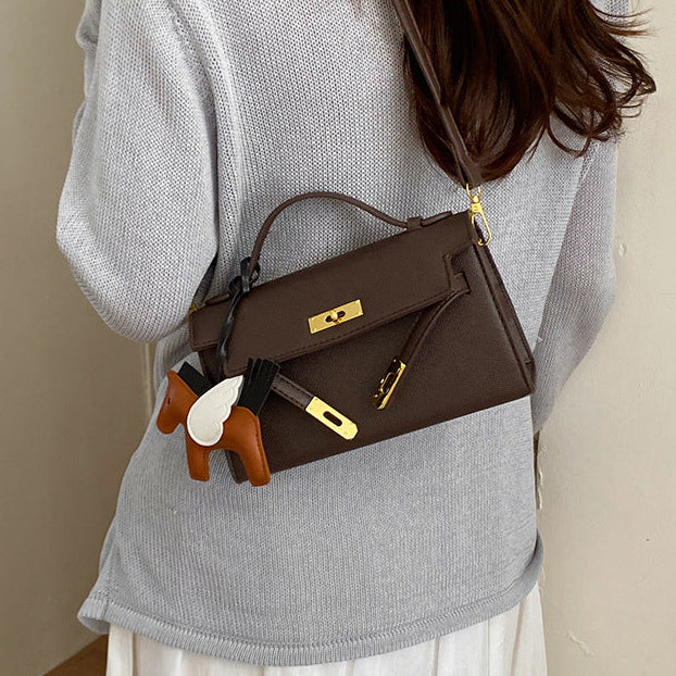 Person wearing a brown handbag with gold hardware on a plain background